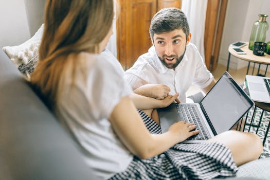 Couple working together from home on laptops, engaged in conversation.