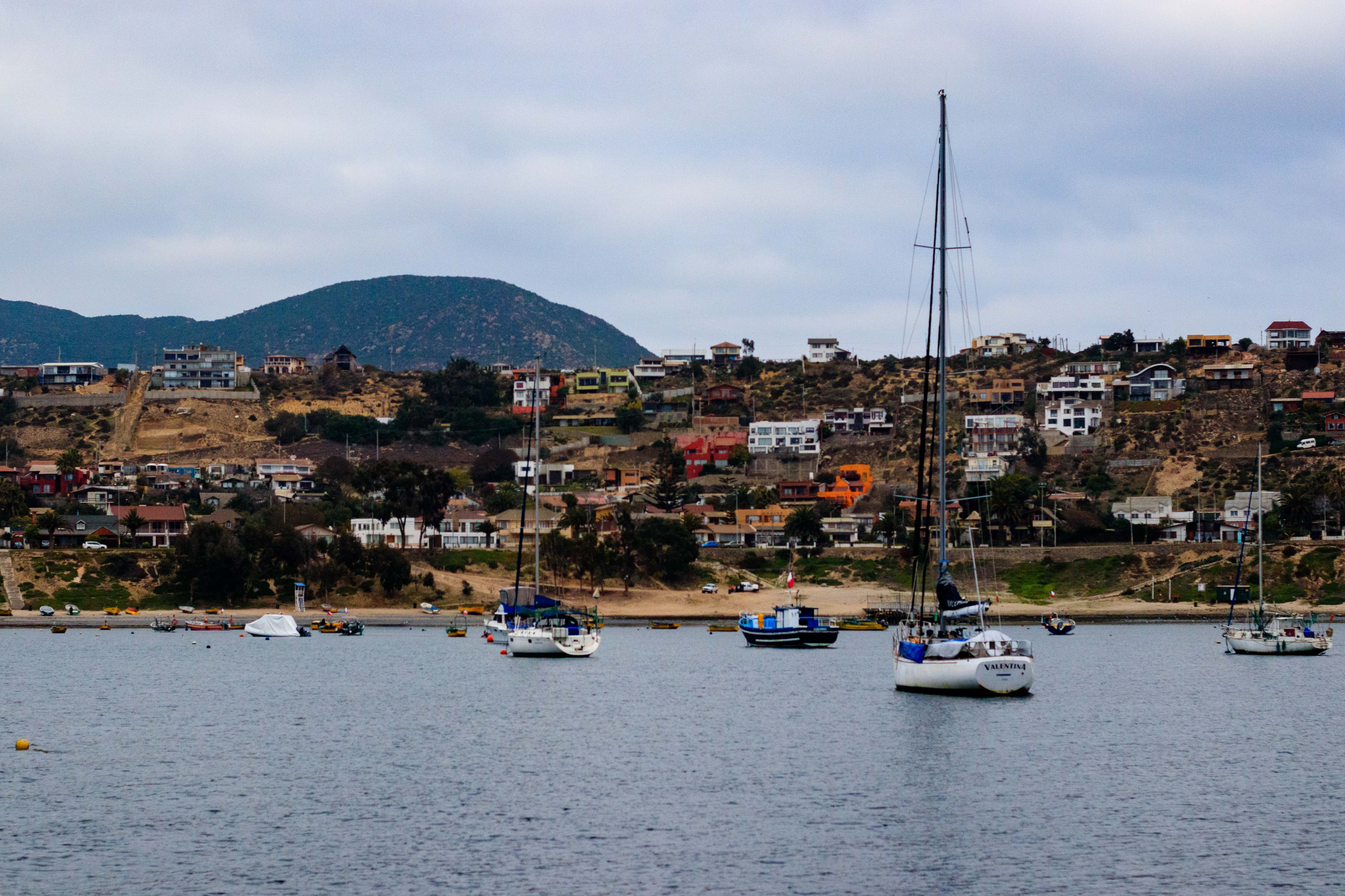 Scenic view of sailboats on water with colorful hillside town and mountains in Chile.