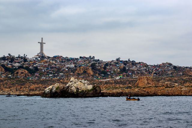 A scenic view of Coquimbo, Chile, showcasing a coastal city with a prominent cross and small fishing boat.