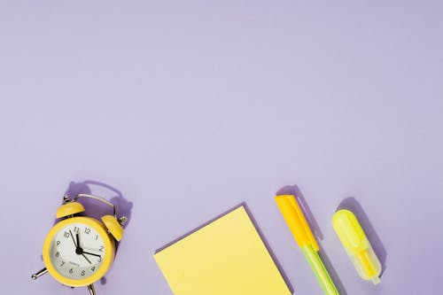 Free Yellow Sticky Note Pad Beside an Alarm Clock and a Ball Pen Stock Photo