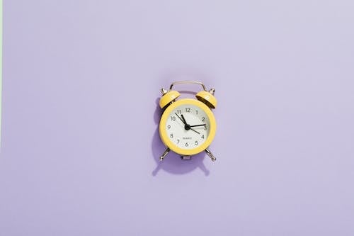 Free Close-Up Shot of a Yellow Alarm Clock on a Purple Surface Stock Photo