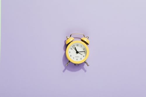 Close-Up Shot of a Yellow Alarm Clock on a Purple Surface