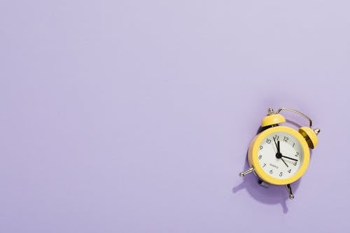 Close-Up Shot of a Yellow Alarm Clock on a Purple Surface