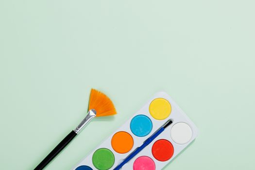 Bright watercolor palette and paintbrush on a soft green background, perfect for artists.
