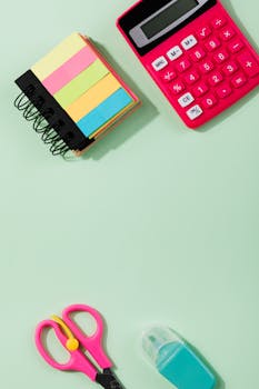 A vibrant collection of school supplies on a green background featuring a calculator, sticky notes, and scissors.