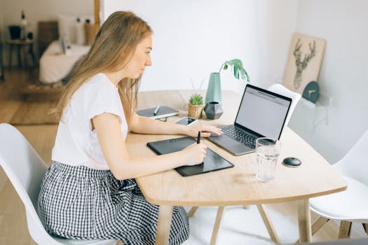 A young woman working remotely at a wooden table with her laptop and tablet in a cozy home setting.