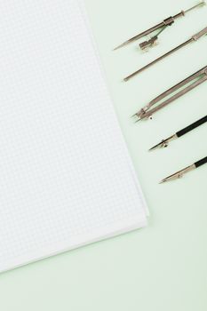 Aesthetic still life of graph paper and drawing compasses on a light green backdrop.