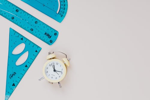 An Analogue Alarm Clock Beside Assorted Rulers on a Surface