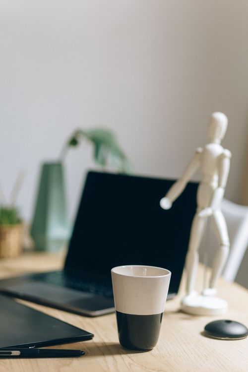 Free Close-up of a desk with laptop, cup, figurine, and decor elements. Stock Photo