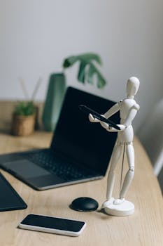 Modern workspace featuring a laptop, figurine, and smartphone on a wooden table.