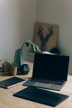 A minimalist workspace featuring a laptop, notebook, and plants on a wooden table.