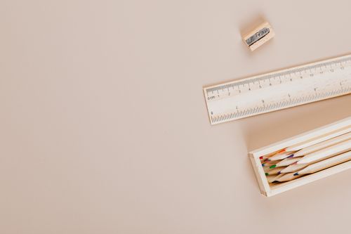 Free Top view of color pencils in a box with a ruler and sharpener on a beige background. Stock Photo