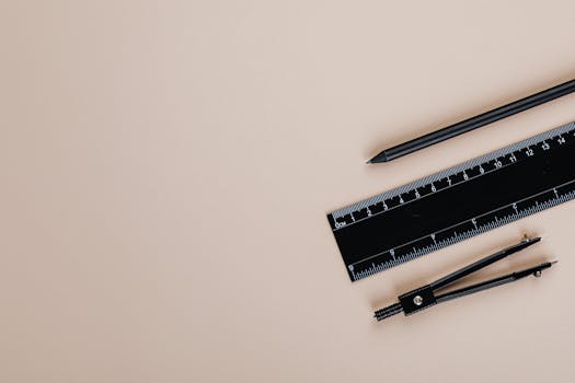 Minimalist flat lay of a compass, pencil, and ruler on a cream-colored background.