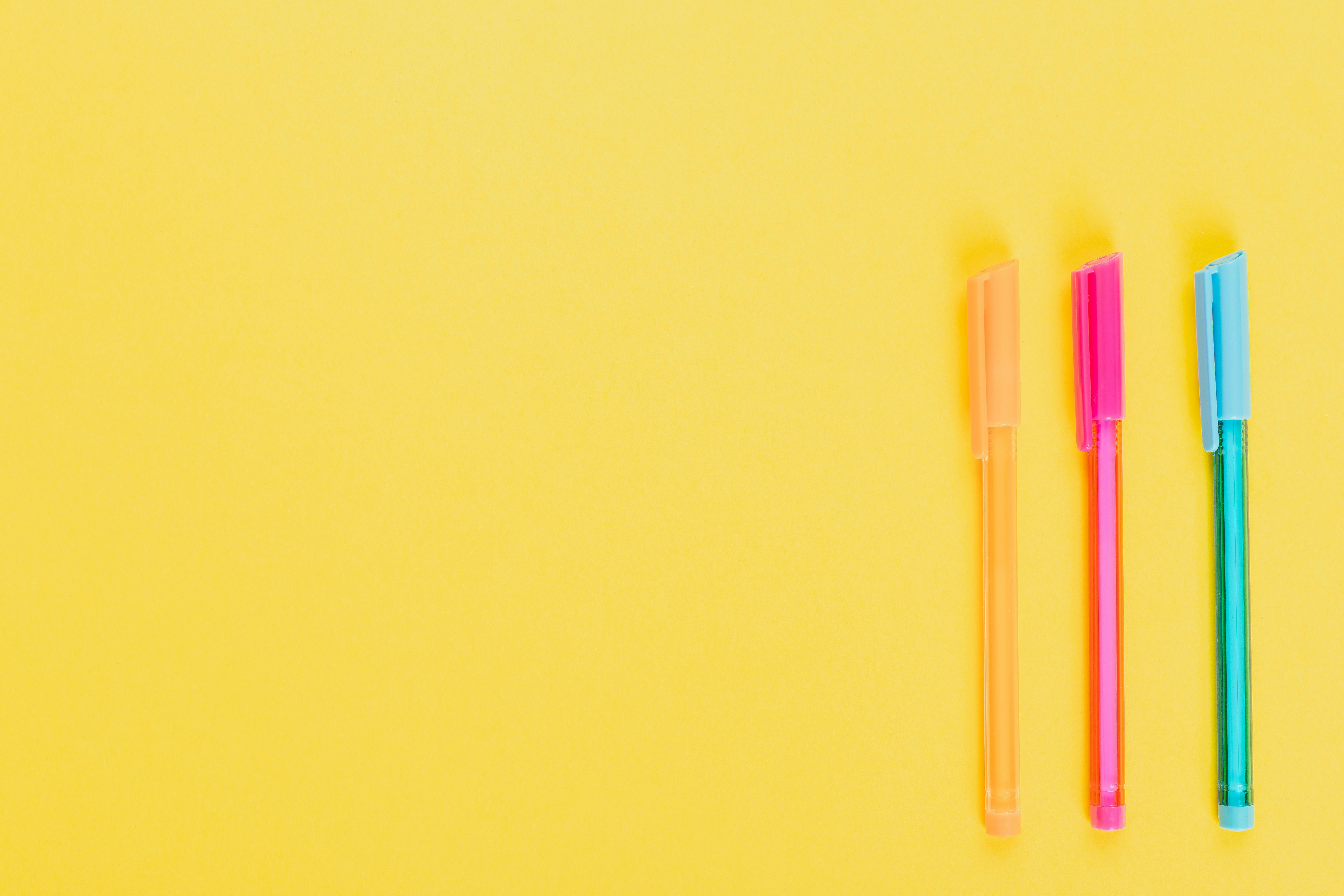 Flatlay of colorful pens against a minimalist yellow backdrop with ample copy space.