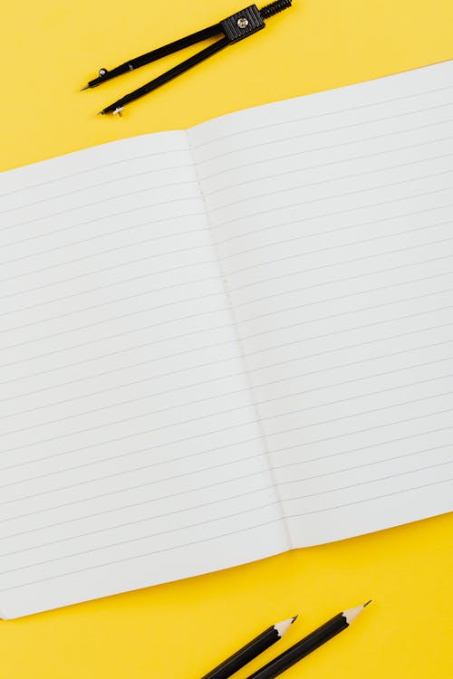 A Notebook Beside Black Pencils and Compass