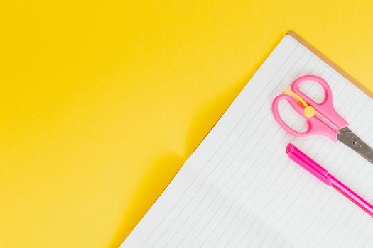A vibrant top view of pink scissors and a pen on a lined notebook with bright yellow background.