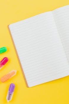 Flat lay of colorful highlighters and an open notebook on a vibrant yellow background.
