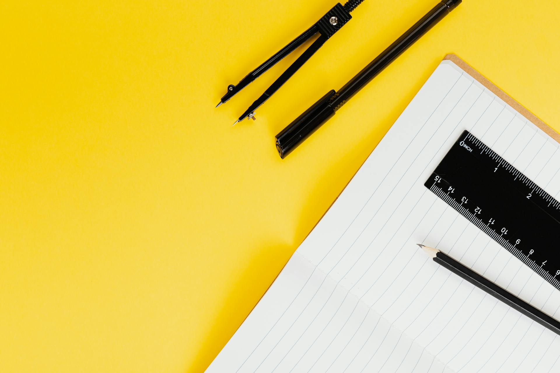 Notebook with pencil, ruler, and compass on a bright yellow background, perfect for education and design themes.