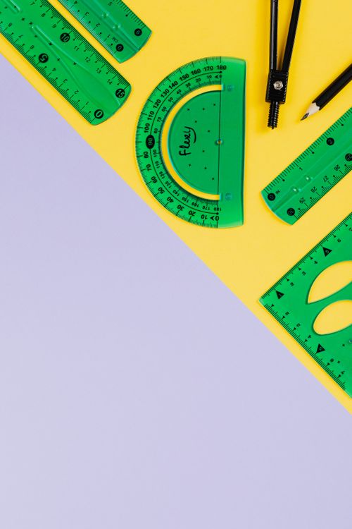 Free Green rulers, compass, and pencils on a yellow and purple background with copy space. Stock Photo