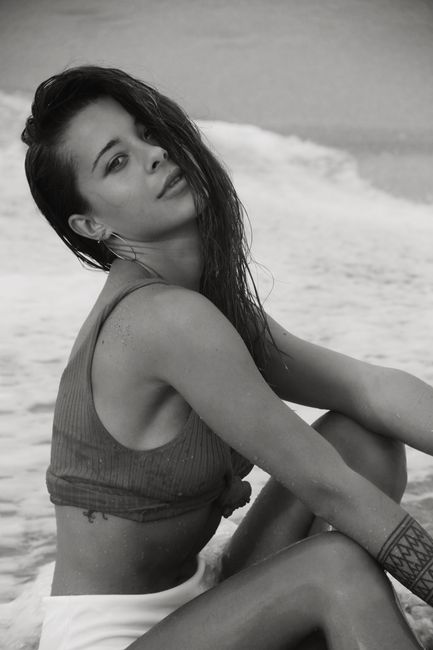 Black and white of young female with long hair in summer clothes sitting on sandy coast near waving sea