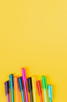 Top view of colorful pens arranged on a bright yellow background with copy space.