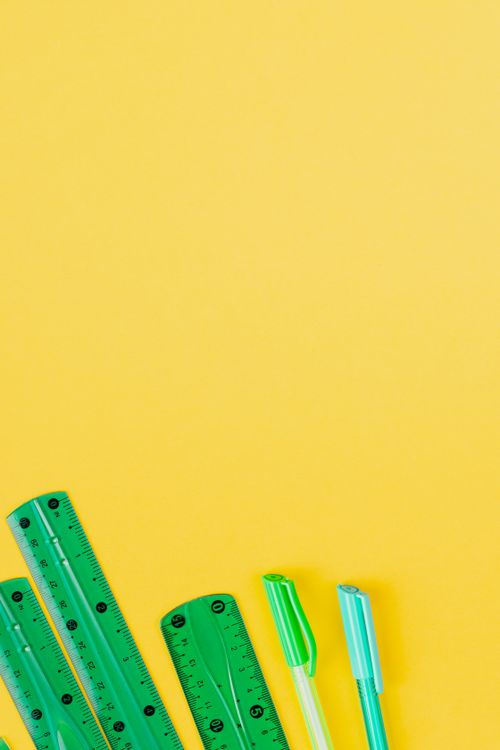 Free Green rulers and pens laid out on a bright yellow background, perfect for educational themes. Stock Photo