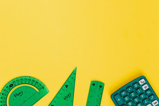 Vibrant school accessories including calculator and rulers against yellow backdrop.