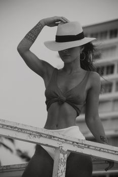 Black and white of anonymous slim  female in swimsuit and hat standing on street against building