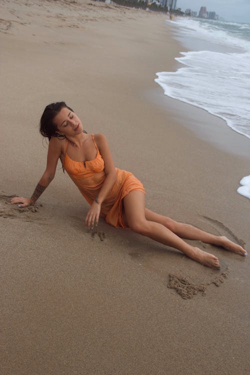 Free From above of slim young female with dark hair in wet tight dress lying on sandy beach near waving sea Stock Photo