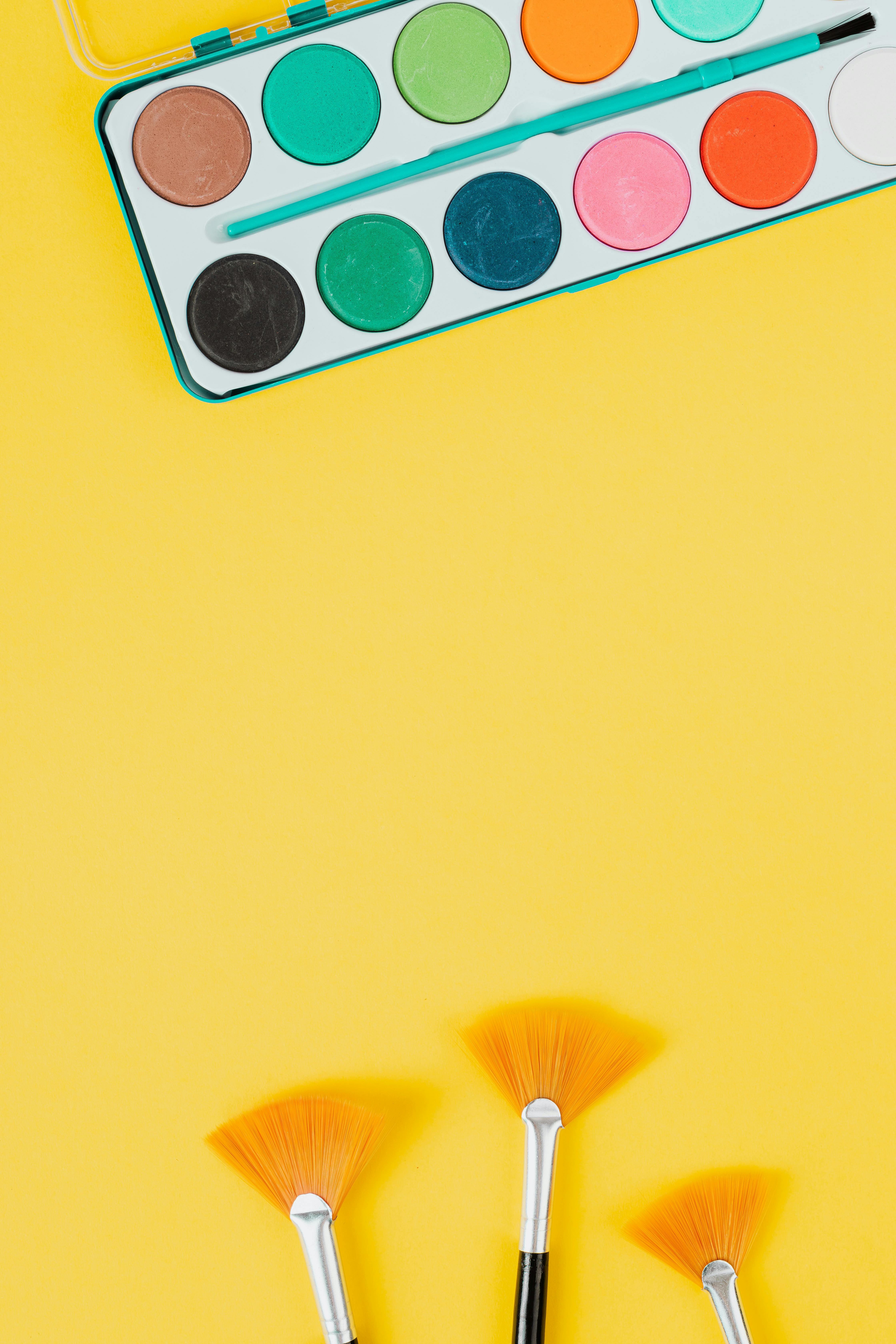 大胆的黄色表面上摆放着充满活力的水彩套装和画笔