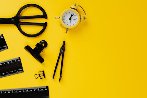 Black School Materials and Yellow Alarm Clock on Yellow Background