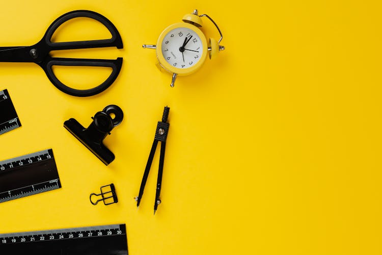 Black School Materials And Yellow Alarm Clock On Yellow Background