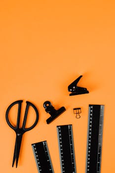 Flat lay of black office supplies on vibrant orange background, ideal for business themes.