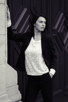 Stylish woman in a black blazer posing against an ornate wall in monochrome.