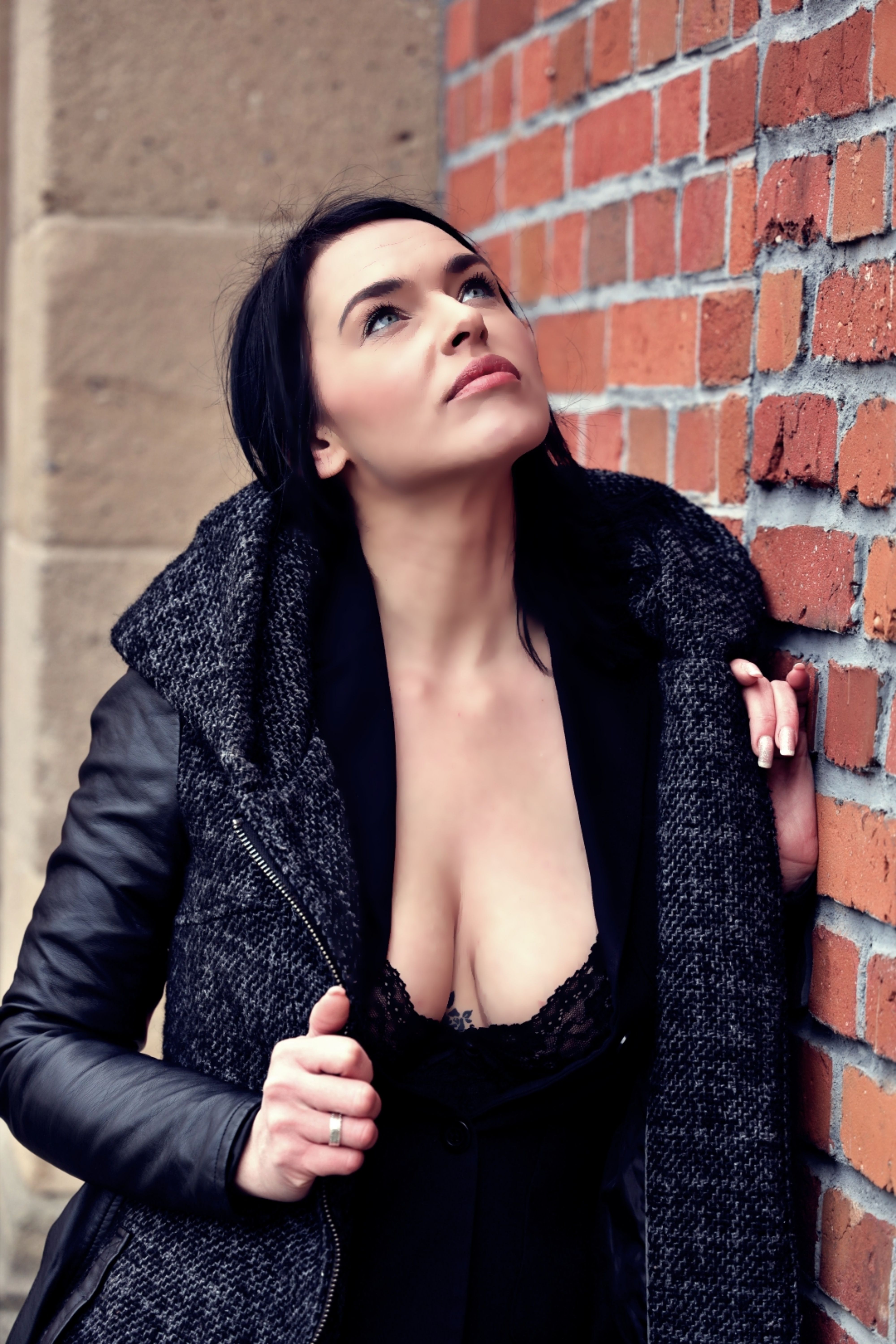 Portrait of an elegant woman in a black leather jacket looking thoughtful by a brick wall.