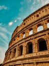 Low angle of ancient Coliseum with arched elements and stone columns under blue sky in Rome