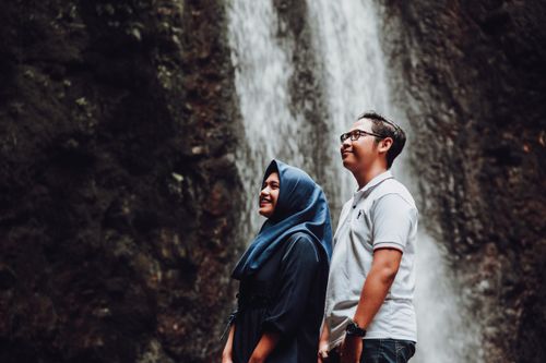 Free A couple stands joyously by a waterfall, embracing nature's beauty. Stock Photo