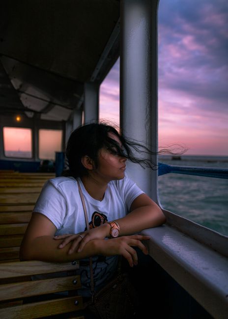 Woman gazes out to sea during a serene ferry ride at sunset, embodying wanderlust.