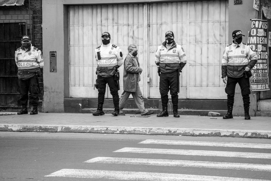 Oficiales de policía y un peatón con mascarilla en escala de grises, manteniendo el distanciamiento social en una calle de la ciudad.