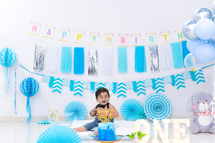 Smiling Little Asian Boy Near Birthday Cake And Decorative Garland