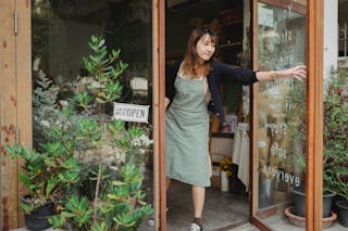Tranquil florist in apron opening glass door of flower shop in daytime in city