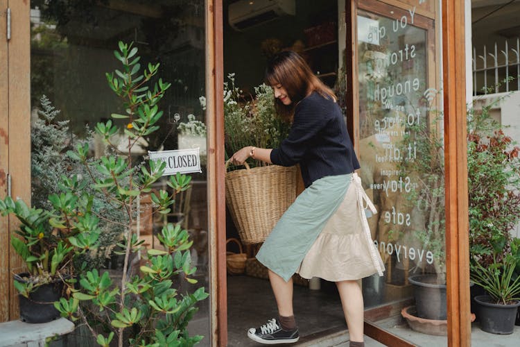 Woman Carrying Basket Into Flower Shop