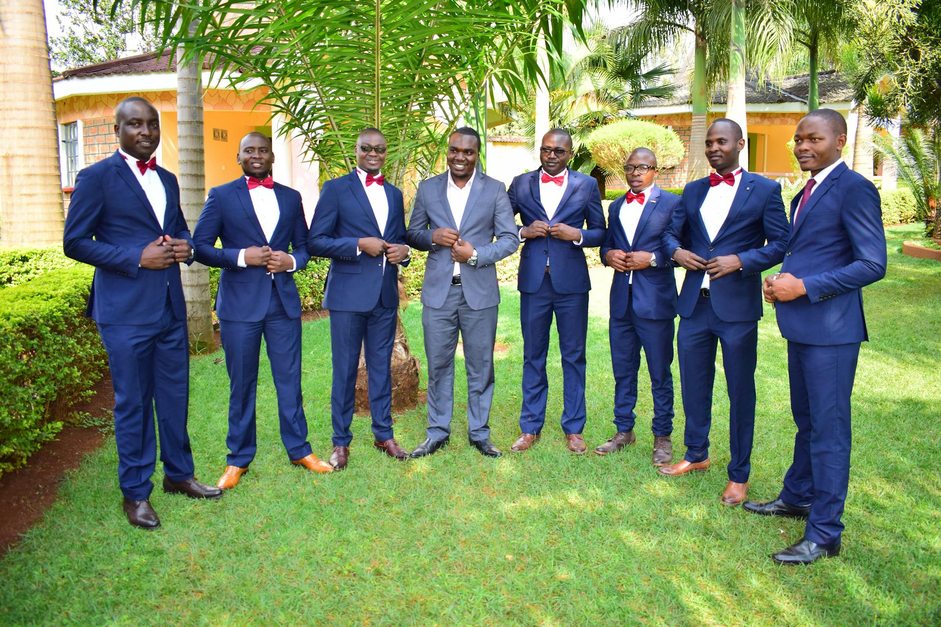 A group of men in formal suits and bow ties standing together in a garden setting.