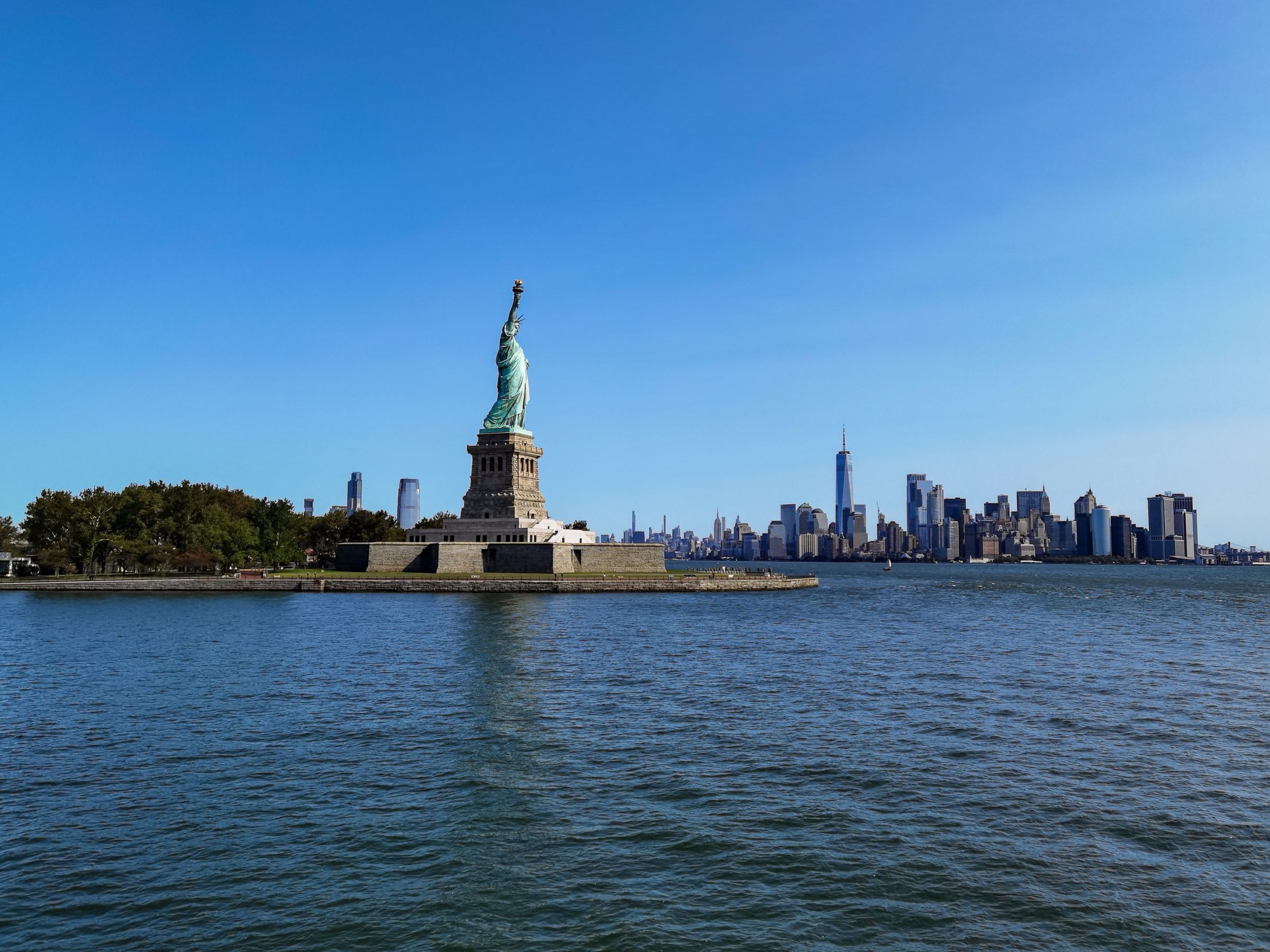 The Statue of Liberty stands before the vibrant New York City skyline on a clear day