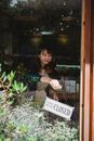 Ethnic woman in casual clothes hanging up sign on door after end of workday