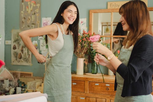 Positive female florists in uniform having conversation and laughing while working in flower shop