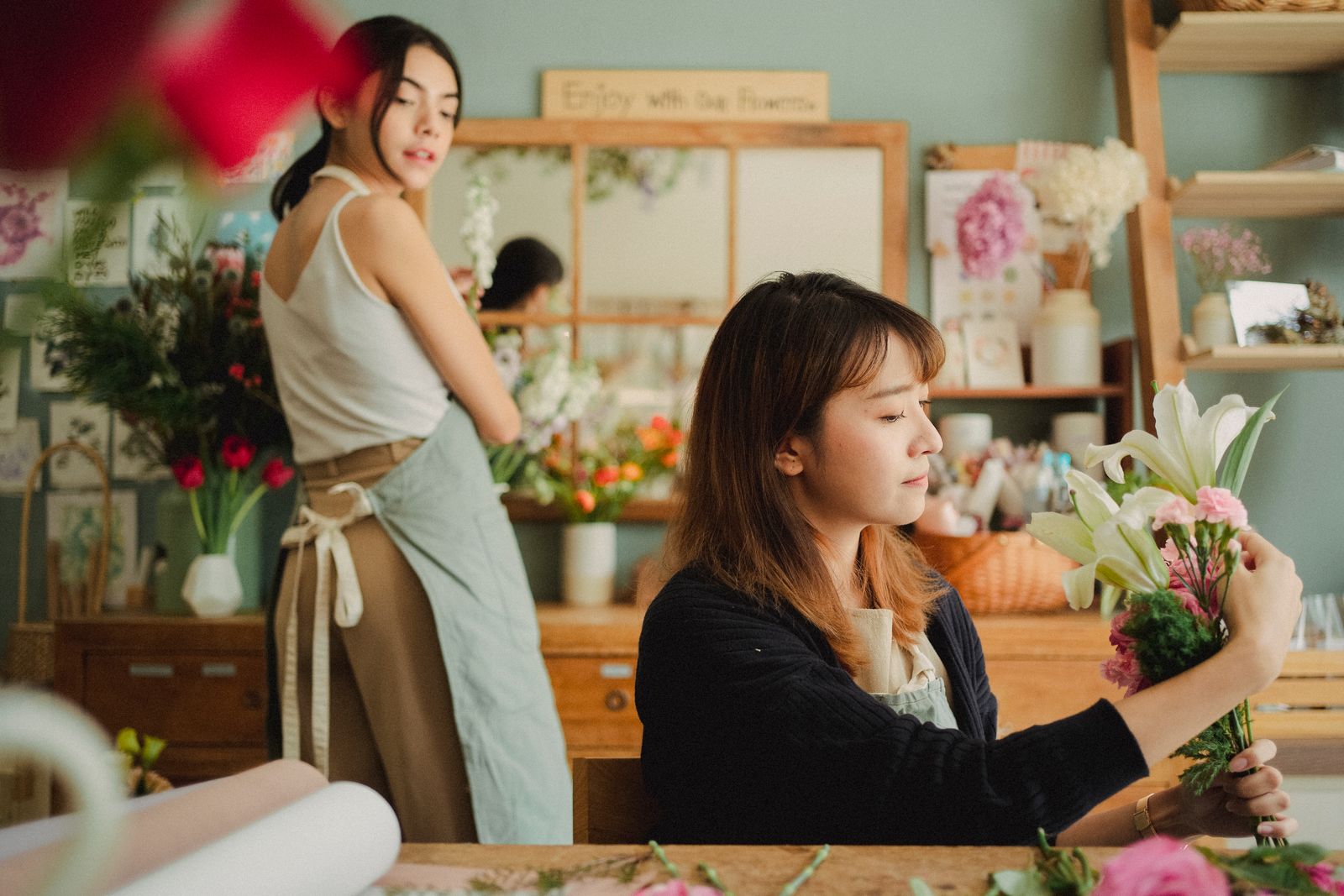Two women making bouquets together in a bright workshop.