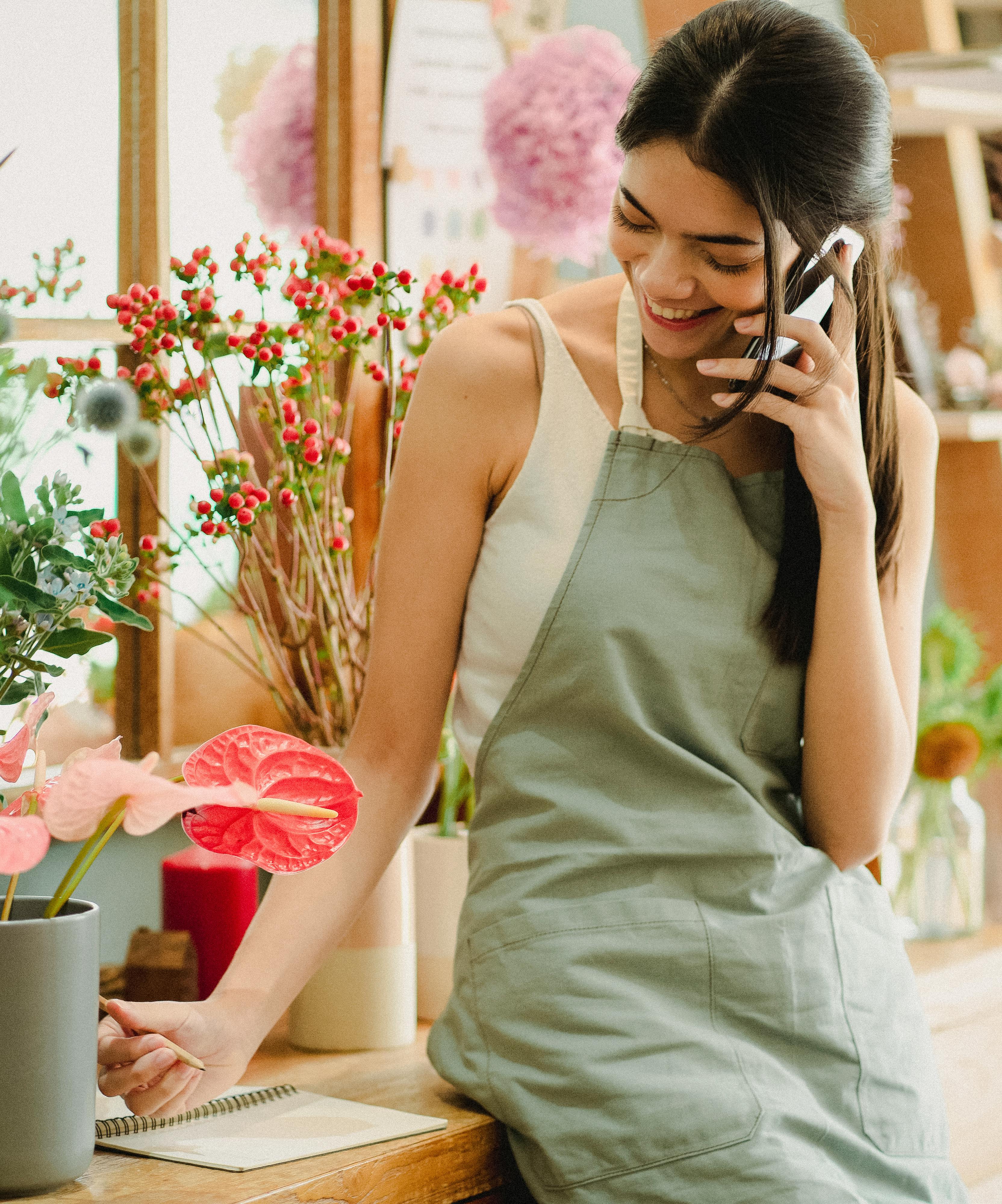 smiling female florist talking on phone in floristry shop