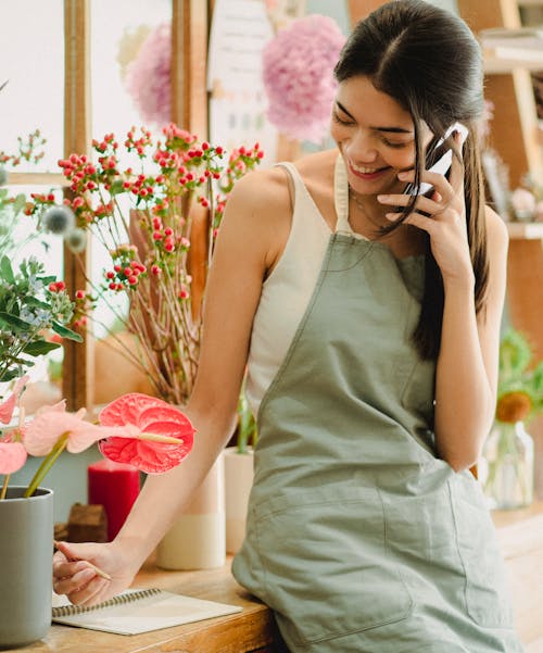 Glimlachende Vrouwelijke Bloemist Die Op Telefoon In Bloemisterijwinkel Spreekt
