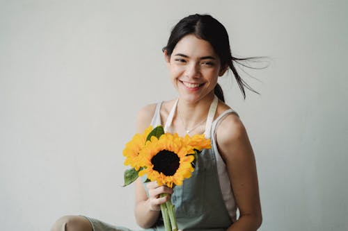 Joyful woman with sunflower bunch standing in light studio